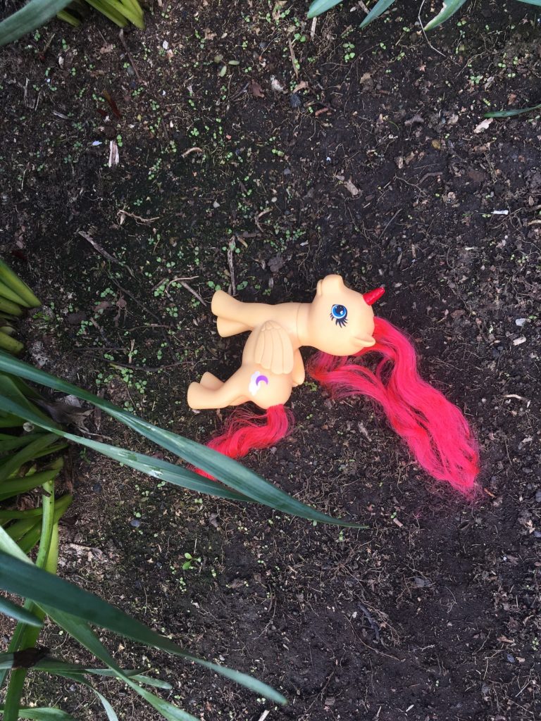 A My Little Pony unicorn with bright red hair lying on fertile ground, shoots sprouting.