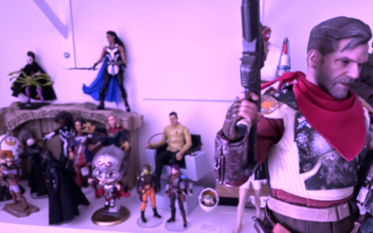 A shelf full of action figures, blurry and out of focus with a significant magenta shift. Hot Toys' rendering of Cobb Vanth is in the foreground far right.