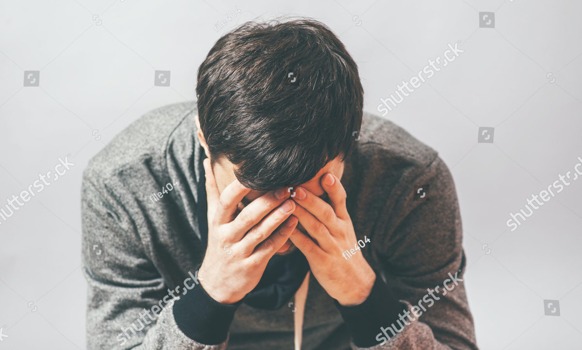 Stock photo (with watermarks intact) of a man in despair, holding his head in his hands