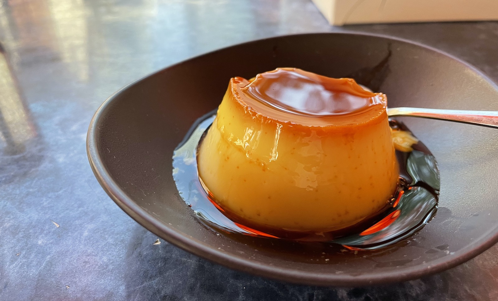 A serving of flan, a yellow custard, sits invitingly on a brown plate.