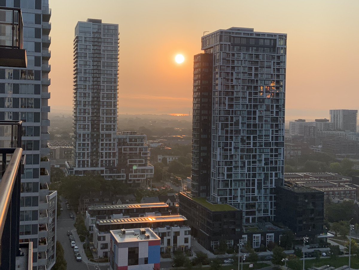 A golden sun rises over Leslieville in Toronto, framed by condo towers. The neighbourhood, partially foggy, is gleaming in the light.