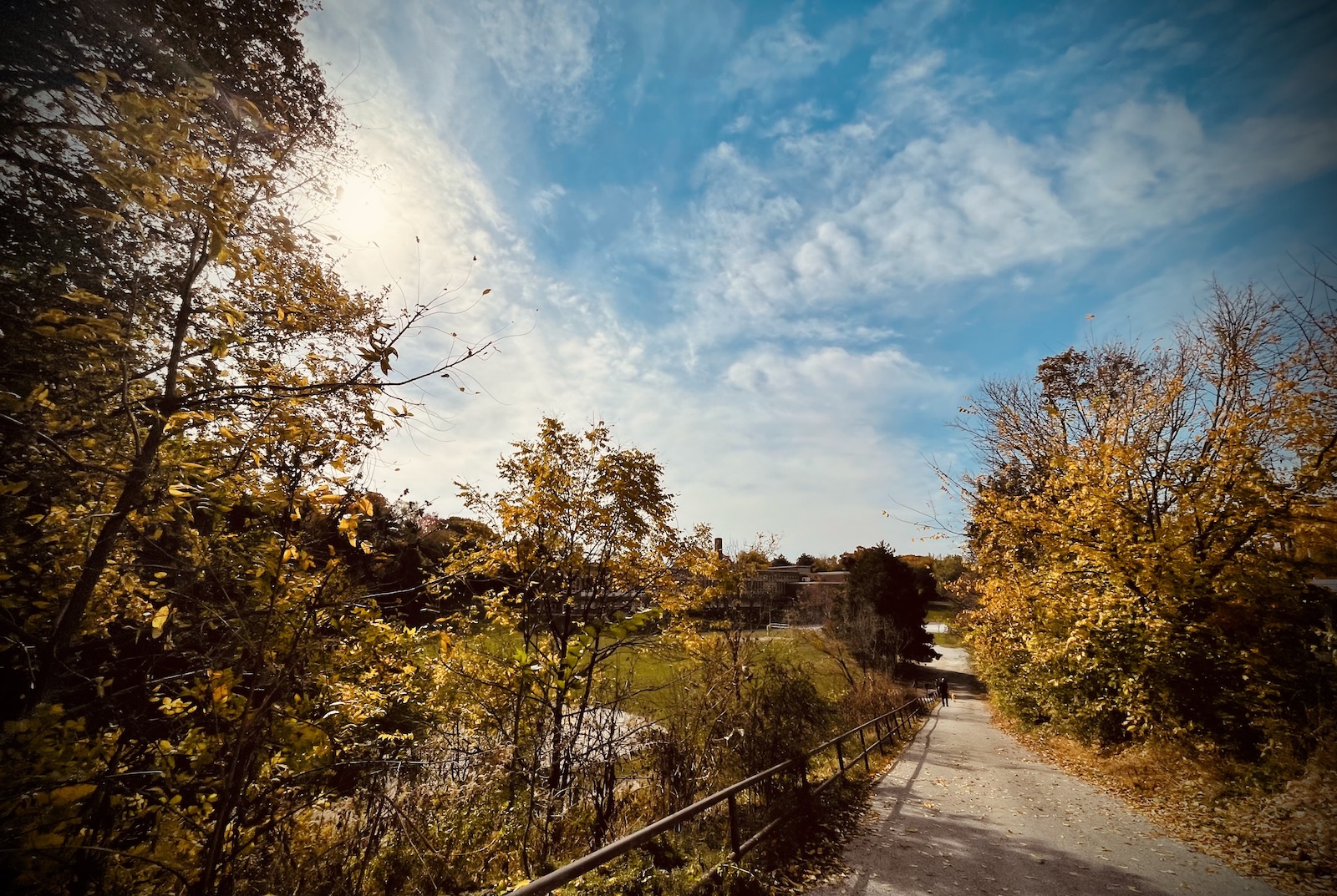 A fisheye image of a wide sky with a blazing sun, hanging over a small autumnal valley with a school barely visible in the distance.